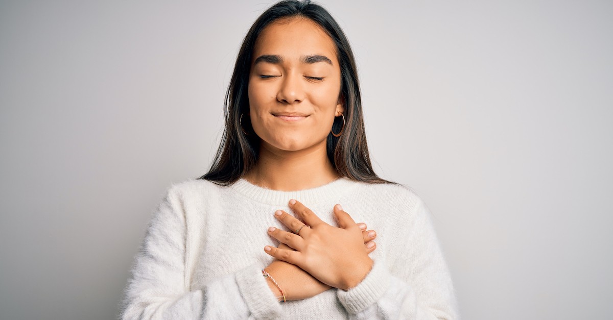 Thankful and grateful woman smiling with eyes closed and prayer hands over heart; underrated Bible verses. 