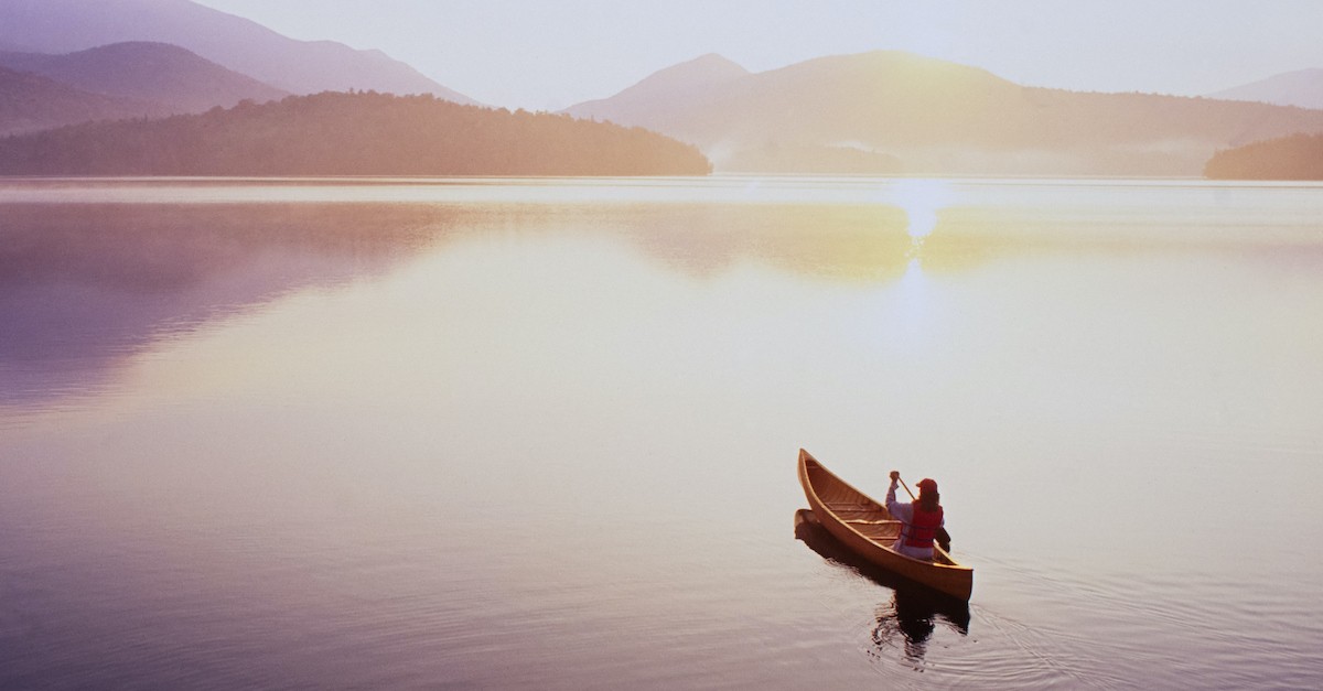 serene lake scene with canoe paddling toward mountainscape