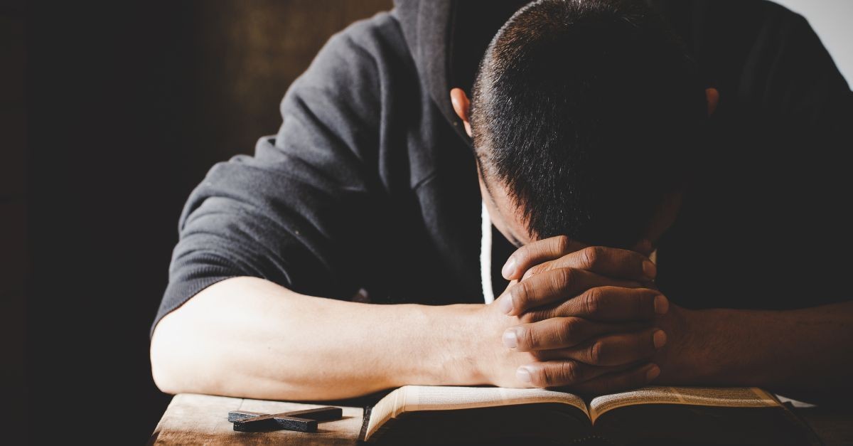 Man humbly praying with his head down on a Bible; difference between knowing about Jesus and having a personal relationship with Him.