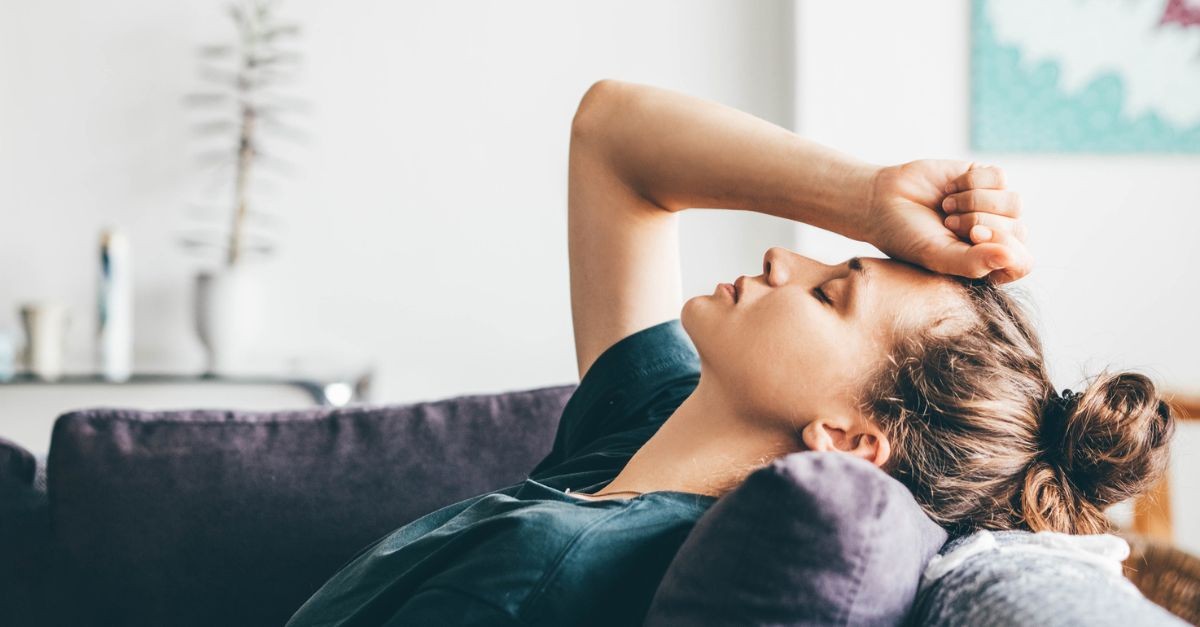 Woman sitting on a couch, reclined back, holding her head with eyes closed; pride is a thief.