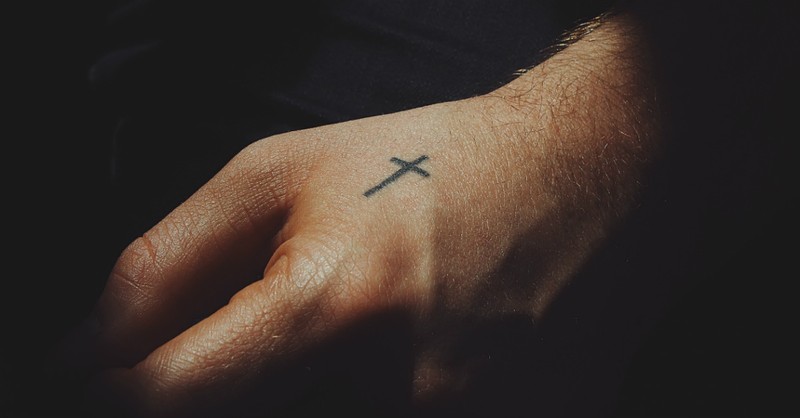 Small cross tattoo on someone's hand